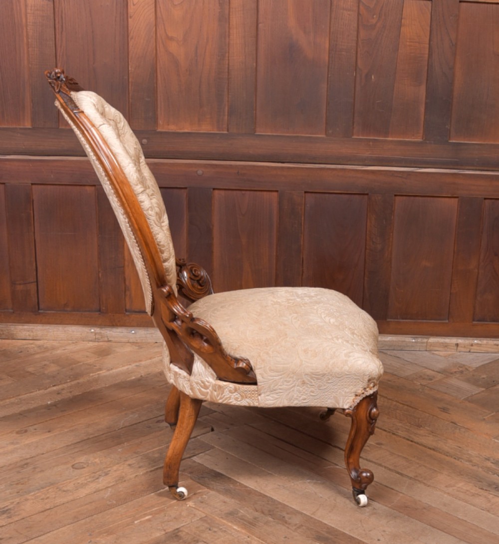 A Victorian carved walnut nursing chair with a button-tufted oval backrest, champagne fabric upholstery, carved cabriole legs, and ceramic castors. View VIII