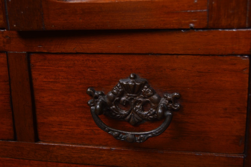 An Edwardian miniature mahogany wardrobe featuring mirrored twin doors, three lower drawers with brass drop handles, and an arched crest inscribed with initials. View XI