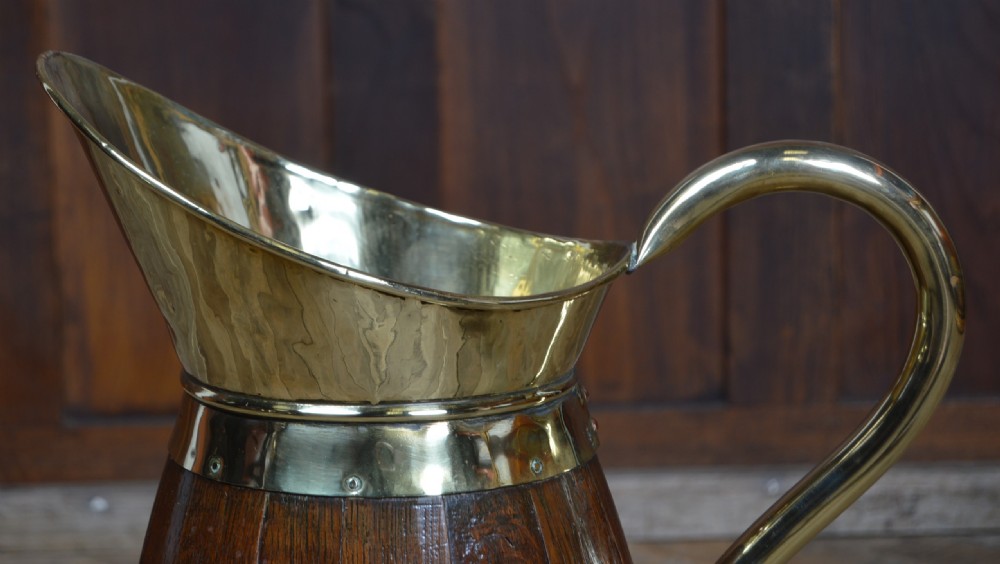 An Edwardian coopered oak jug featuring dark wooden staves bound by polished brass straps, a brass spout liner, and a swept brass handle. View V