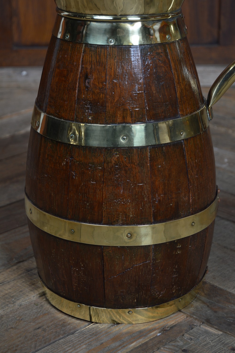 An Edwardian coopered oak jug featuring dark wooden staves bound by polished brass straps, a brass spout liner, and a swept brass handle. View VI