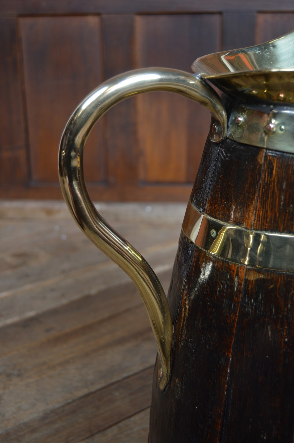 An Edwardian coopered dark oak jug featuring horizontal brass binding bands, a brass lined flared spout, and a curved brass handle. View III