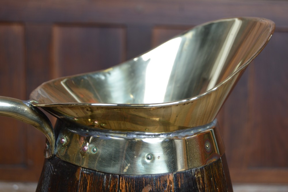 An Edwardian coopered dark oak jug featuring horizontal brass binding bands, a brass lined flared spout, and a curved brass handle. View IV