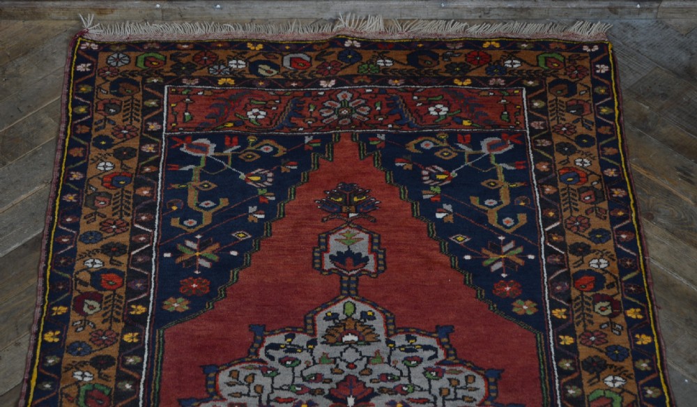A long hand-knotted Turkish rug runner featuring a central light grey and blue geometric medallion on a terracotta red field, framed by dark navy spandrels and a multi-band decorative border. View III