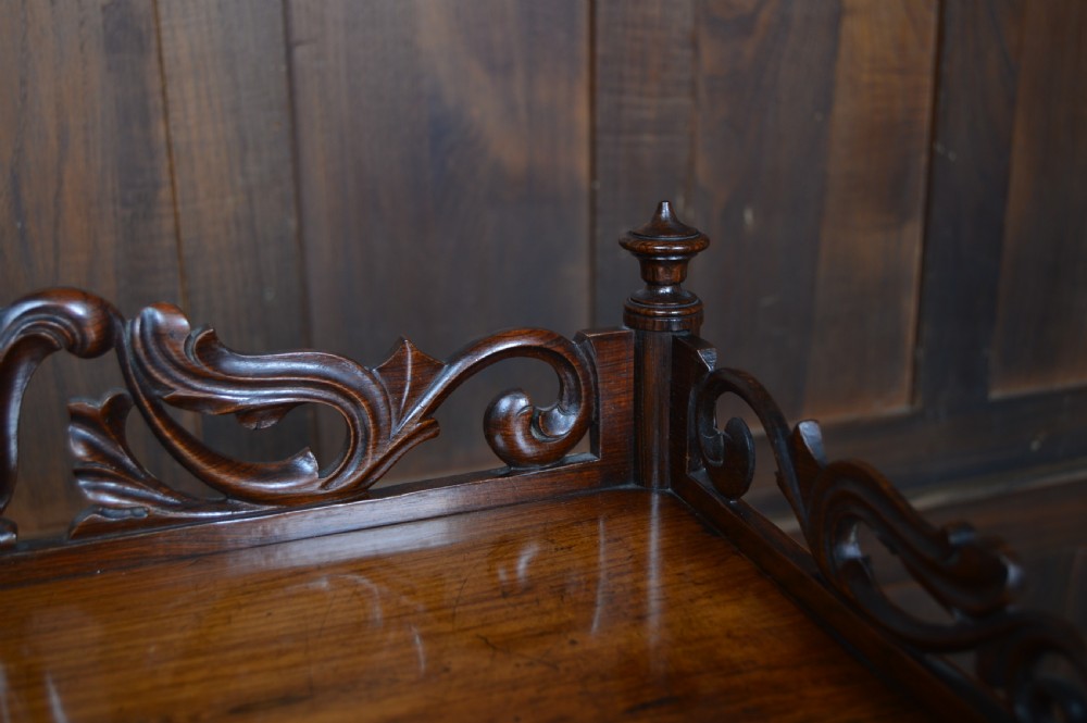 A three-tier Victorian rosewood whatnot featuring turned spindle supports, a carved cresting gallery back, shaped shelf edges, and brass castors. View VI