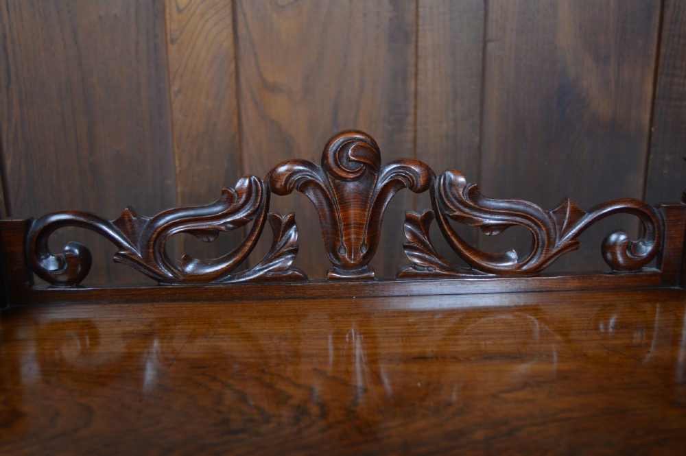 A three-tier Victorian rosewood whatnot featuring turned spindle supports, a carved cresting gallery back, shaped shelf edges, and brass castors. View VII