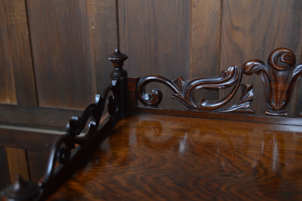 A three-tier Victorian rosewood whatnot featuring turned spindle supports, a carved cresting gallery back, shaped shelf edges, and brass castors. View VIII