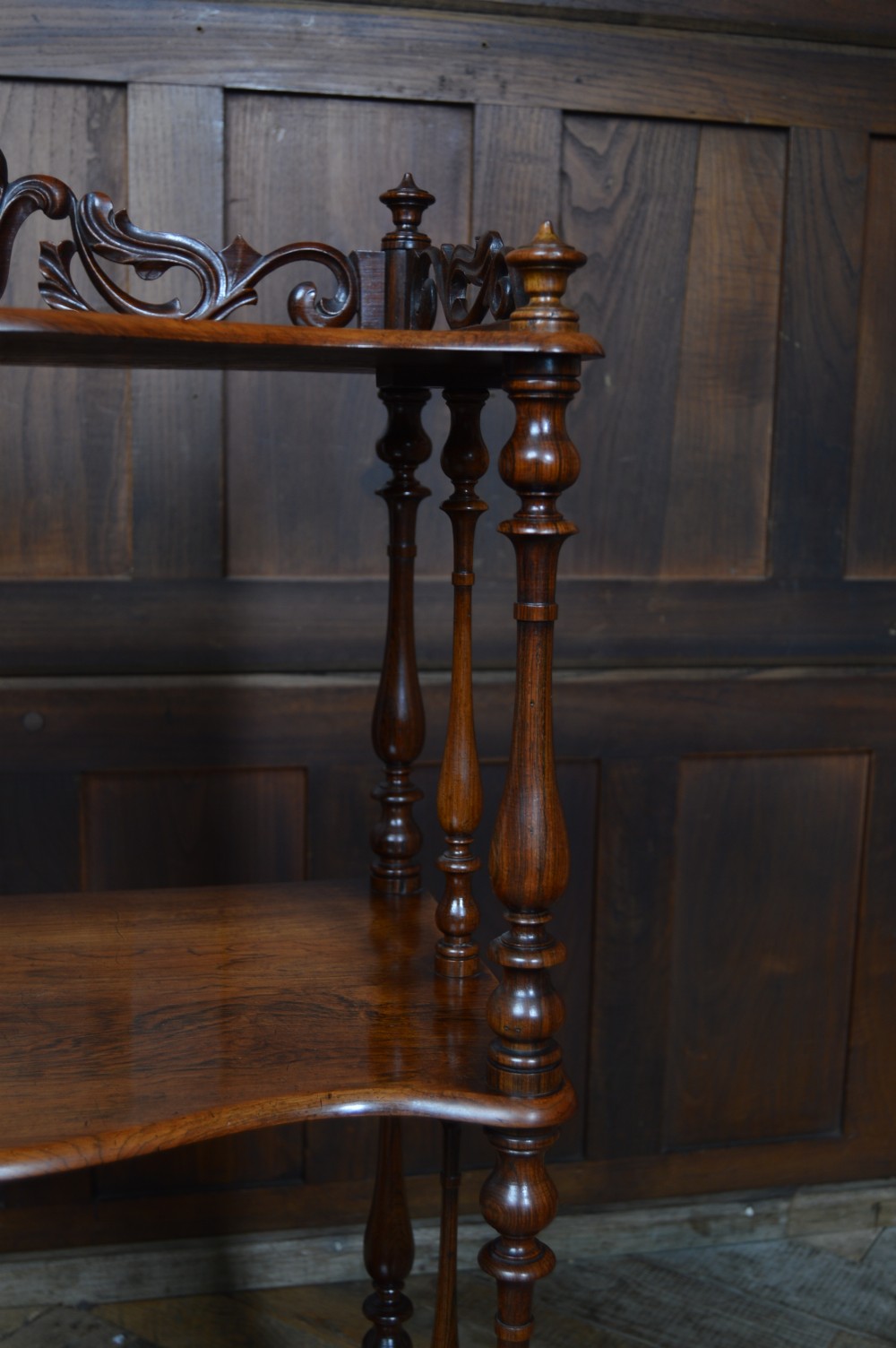 A three-tier Victorian rosewood whatnot featuring turned spindle supports, a carved cresting gallery back, shaped shelf edges, and brass castors. View IX