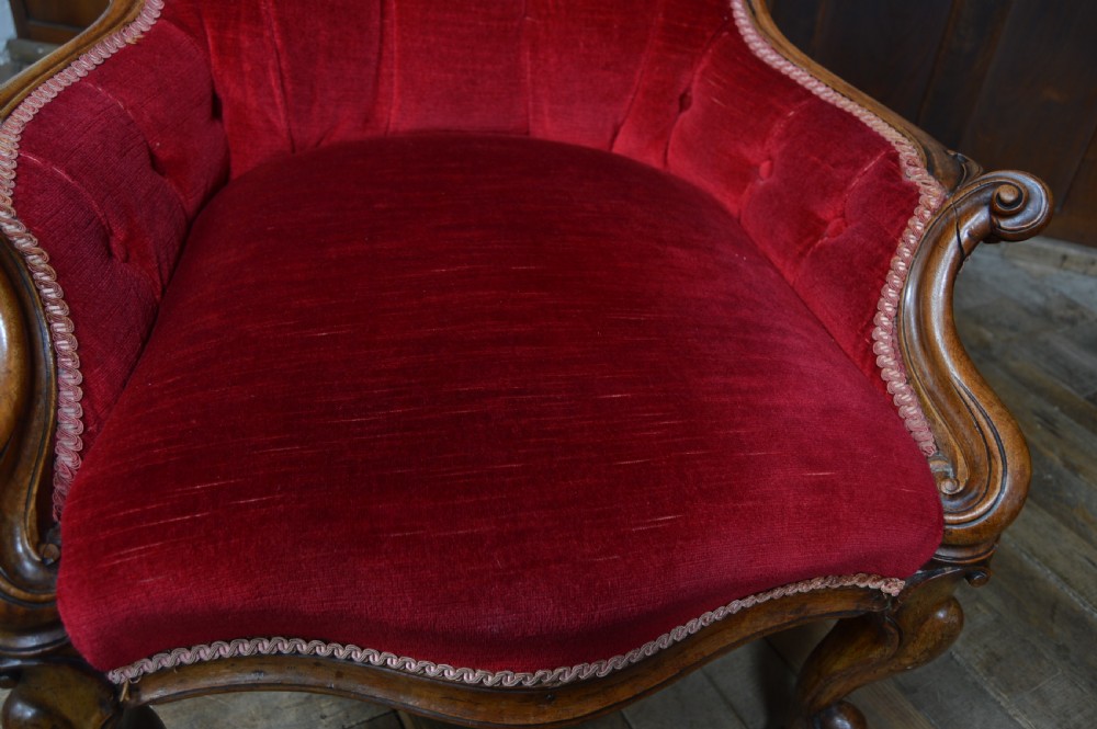 A Victorian walnut parlour armchair with crimson red velvet button-backed upholstery, carved cabriole front legs, and brass castors. View X