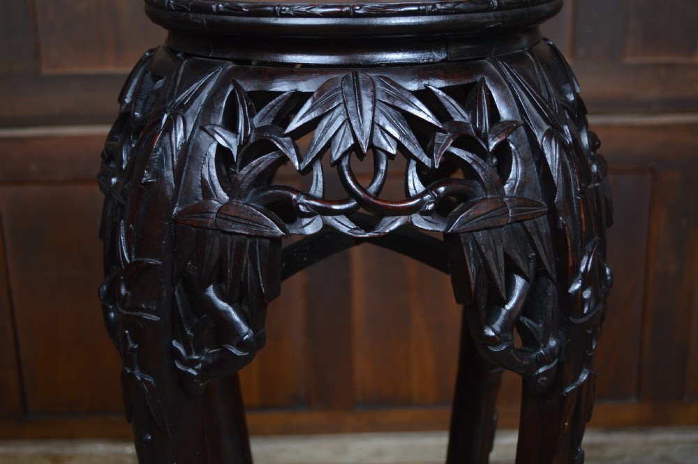 A tall dark carved hardwood stand featuring an inset circular pink marble top and intricate bamboo motif carvings along the apron and legs. View V