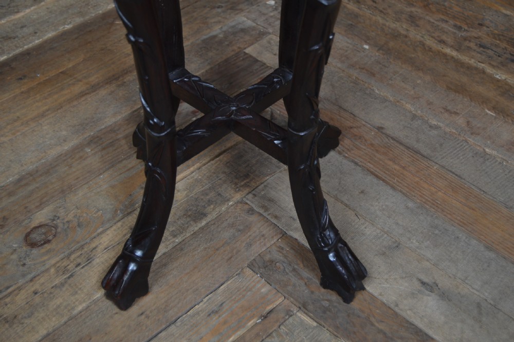 A tall dark carved hardwood stand featuring an inset circular pink marble top and intricate bamboo motif carvings along the apron and legs. View VI