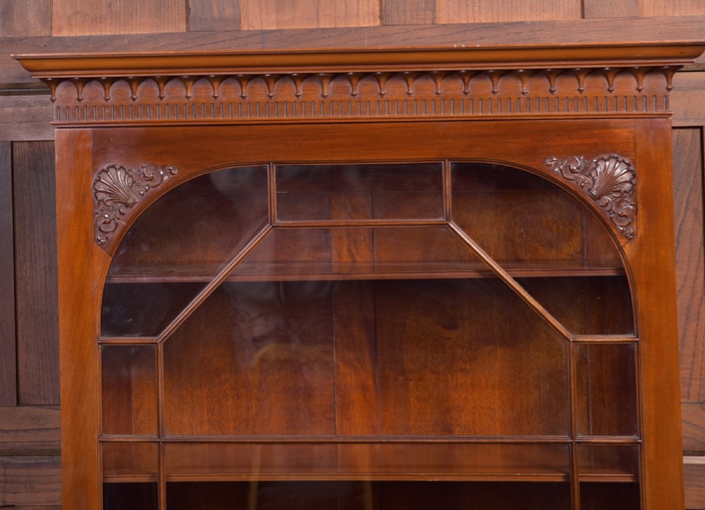 An Edwardian mahogany glazed bookcase featuring geometric astragal glazing, carved corner spandrels, and bottom drawers with drop handles. View III