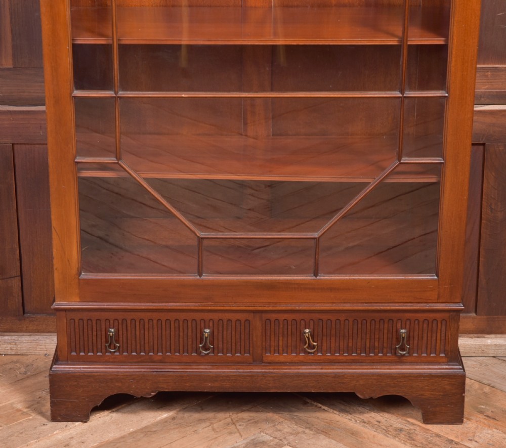An Edwardian mahogany glazed bookcase featuring geometric astragal glazing, carved corner spandrels, and bottom drawers with drop handles. View V