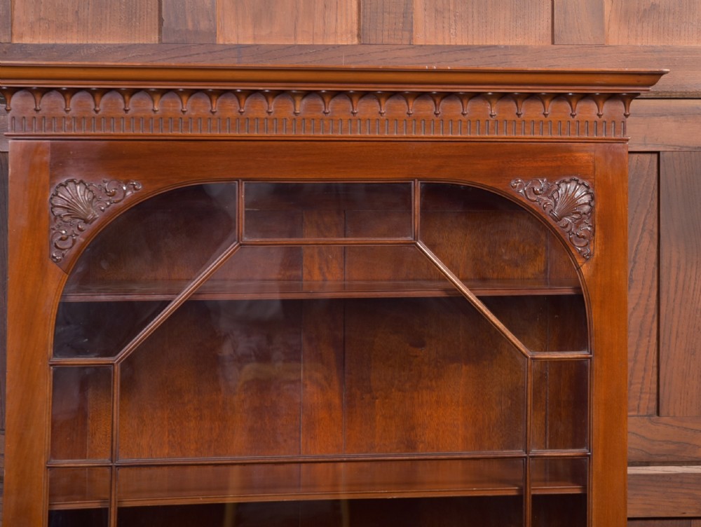 An Edwardian mahogany glazed bookcase featuring geometric astragal glazing, carved corner spandrels, and bottom drawers with drop handles. View VI