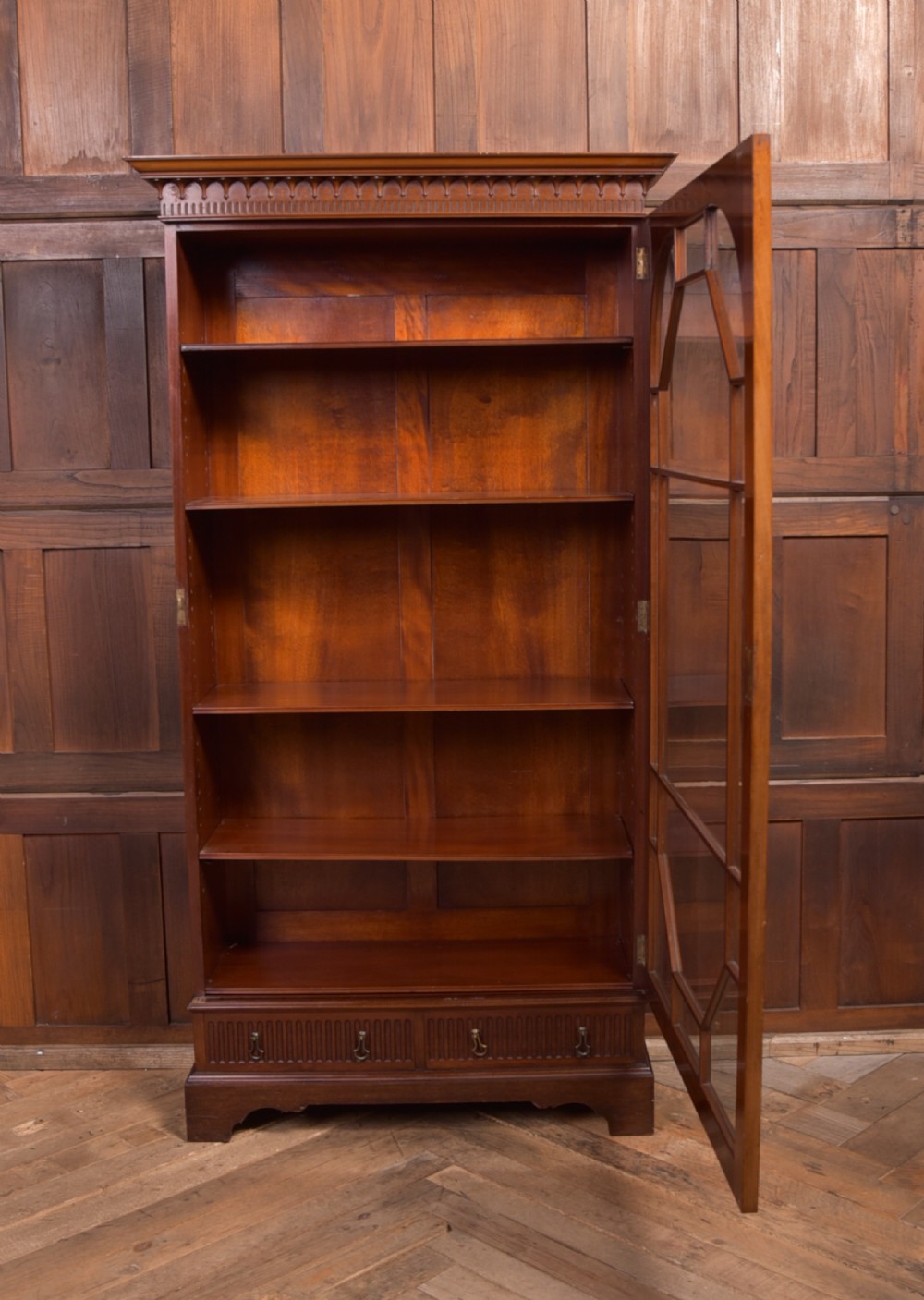 An Edwardian mahogany glazed bookcase featuring geometric astragal glazing, carved corner spandrels, and bottom drawers with drop handles. View XI