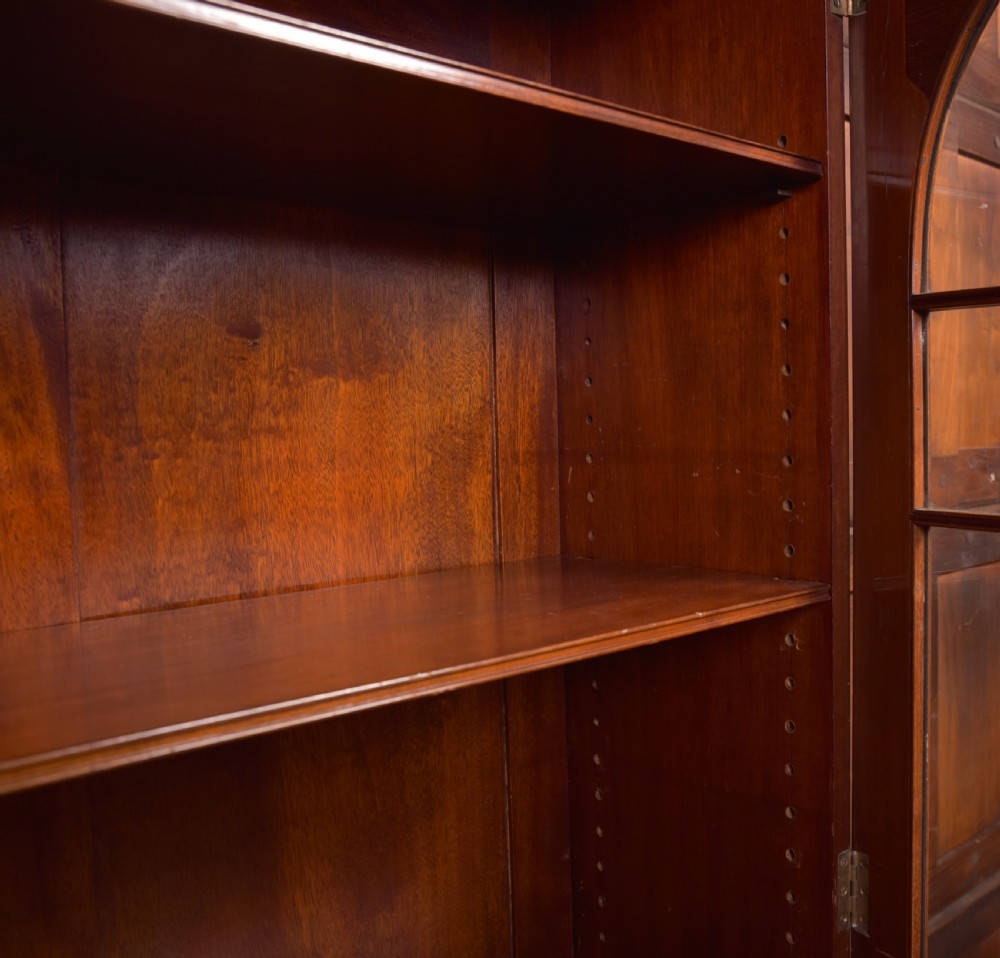 An Edwardian mahogany glazed bookcase featuring geometric astragal glazing, carved corner spandrels, and bottom drawers with drop handles. View XII