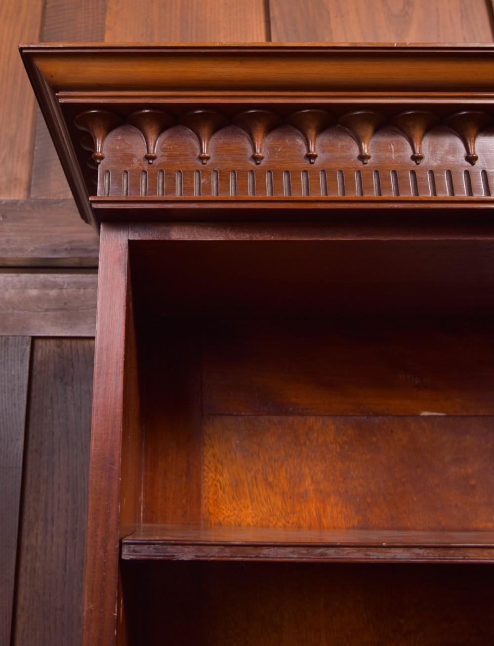 An Edwardian mahogany glazed bookcase featuring geometric astragal glazing, carved corner spandrels, and bottom drawers with drop handles. View XIII