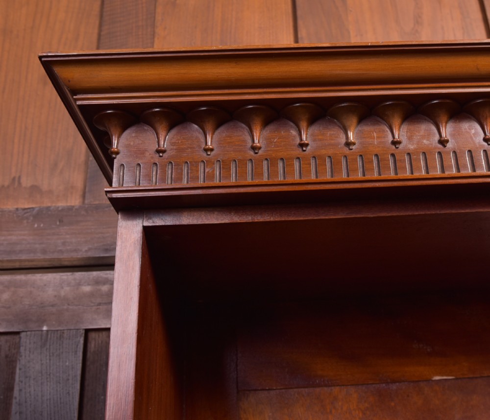 An Edwardian mahogany glazed bookcase featuring geometric astragal glazing, carved corner spandrels, and bottom drawers with drop handles. View XIV