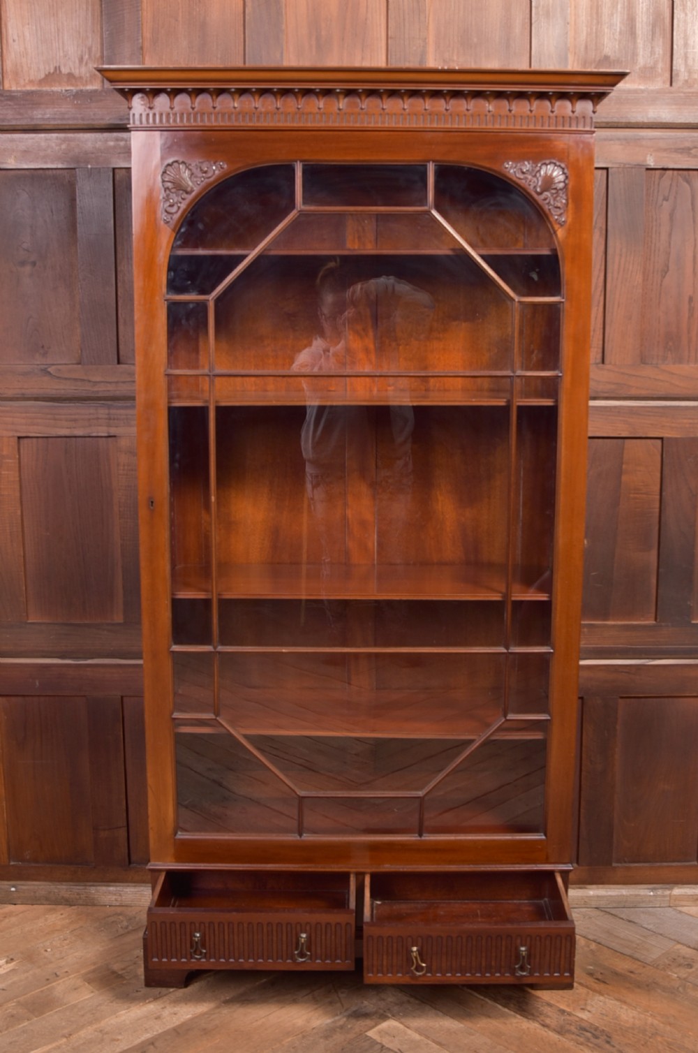 An Edwardian mahogany glazed bookcase featuring geometric astragal glazing, carved corner spandrels, and bottom drawers with drop handles. View XVIII