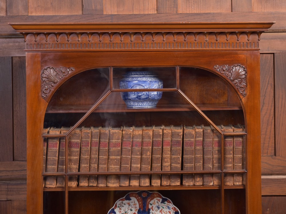 An Edwardian mahogany glazed bookcase featuring geometric astragal glazing, carved corner spandrels, and bottom drawers with drop handles. View XXIV
