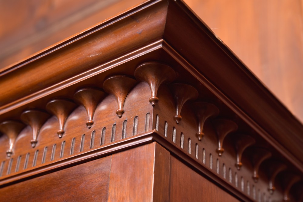 An Edwardian mahogany glazed bookcase featuring geometric astragal glazing, carved corner spandrels, and bottom drawers with drop handles. View XXVI