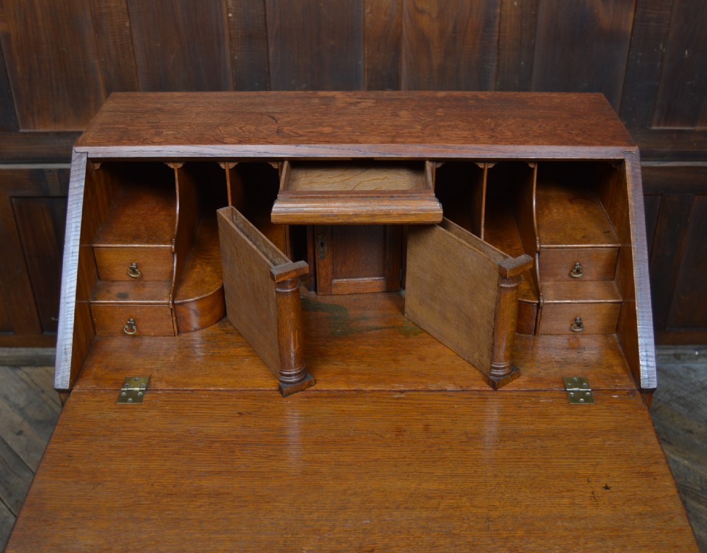An Edwardian oak slant-front bureau on stand featuring brass drop handles, a shaped lower apron, and four cabriole legs ending in pad feet. View V