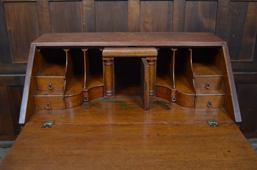 An Edwardian oak slant-front bureau on stand featuring brass drop handles, a shaped lower apron, and four cabriole legs ending in pad feet. View VI