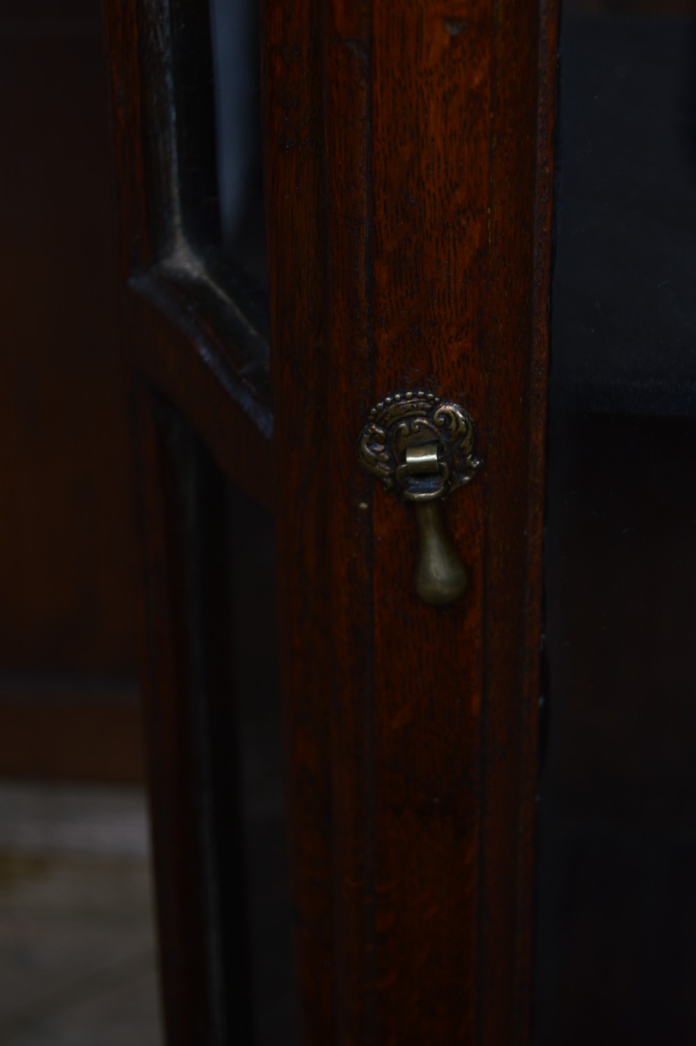 A dark oak tabletop display cabinet featuring an arched pediment, glazed front door with a brass teardrop handle, and glazed side panels. View III