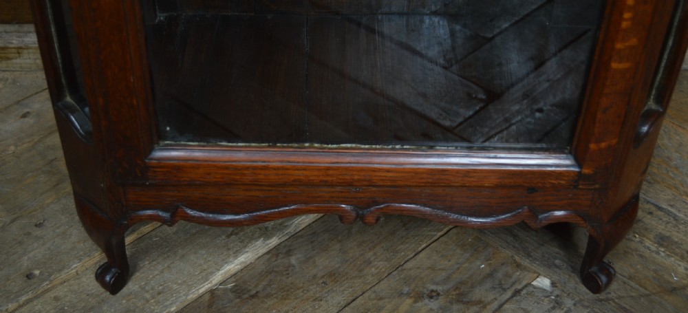 A dark oak tabletop display cabinet featuring an arched pediment, glazed front door with a brass teardrop handle, and glazed side panels. View VI