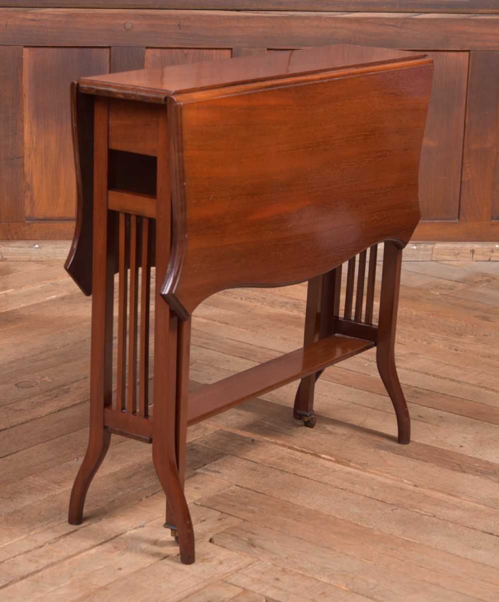 An Edwardian mahogany Sutherland side table shown in a folded state with deep drop leaves, slatted end supports, and curved legs with brass castors. View II
