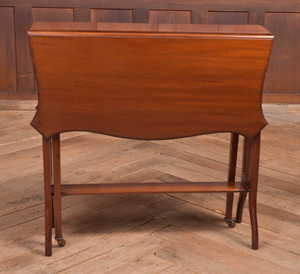 An Edwardian mahogany Sutherland side table shown in a folded state with deep drop leaves, slatted end supports, and curved legs with brass castors. View V