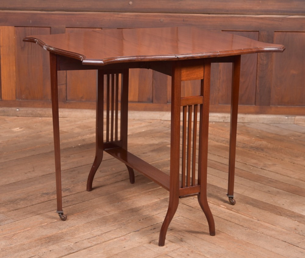 An Edwardian mahogany Sutherland side table shown in a folded state with deep drop leaves, slatted end supports, and curved legs with brass castors. View VIII
