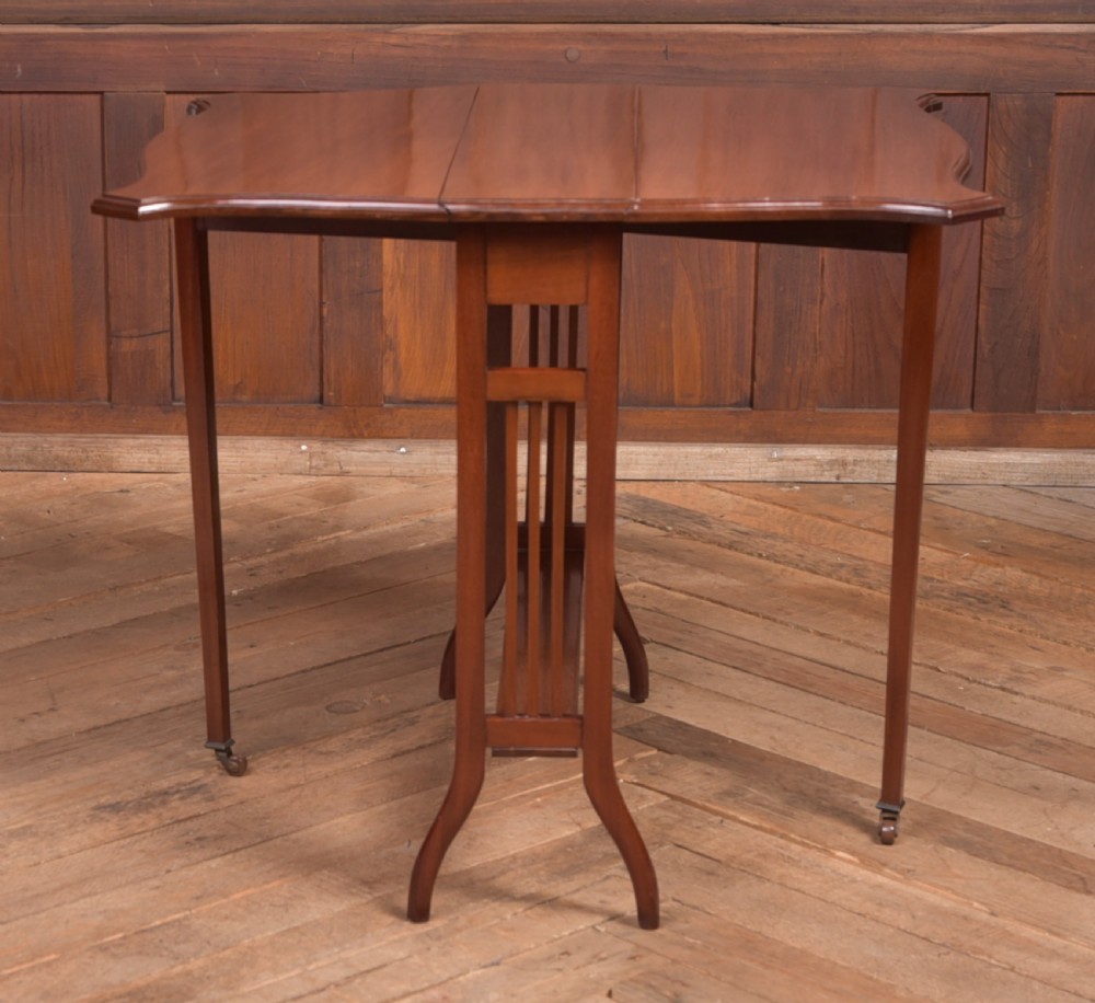 An Edwardian mahogany Sutherland side table shown in a folded state with deep drop leaves, slatted end supports, and curved legs with brass castors. View IX