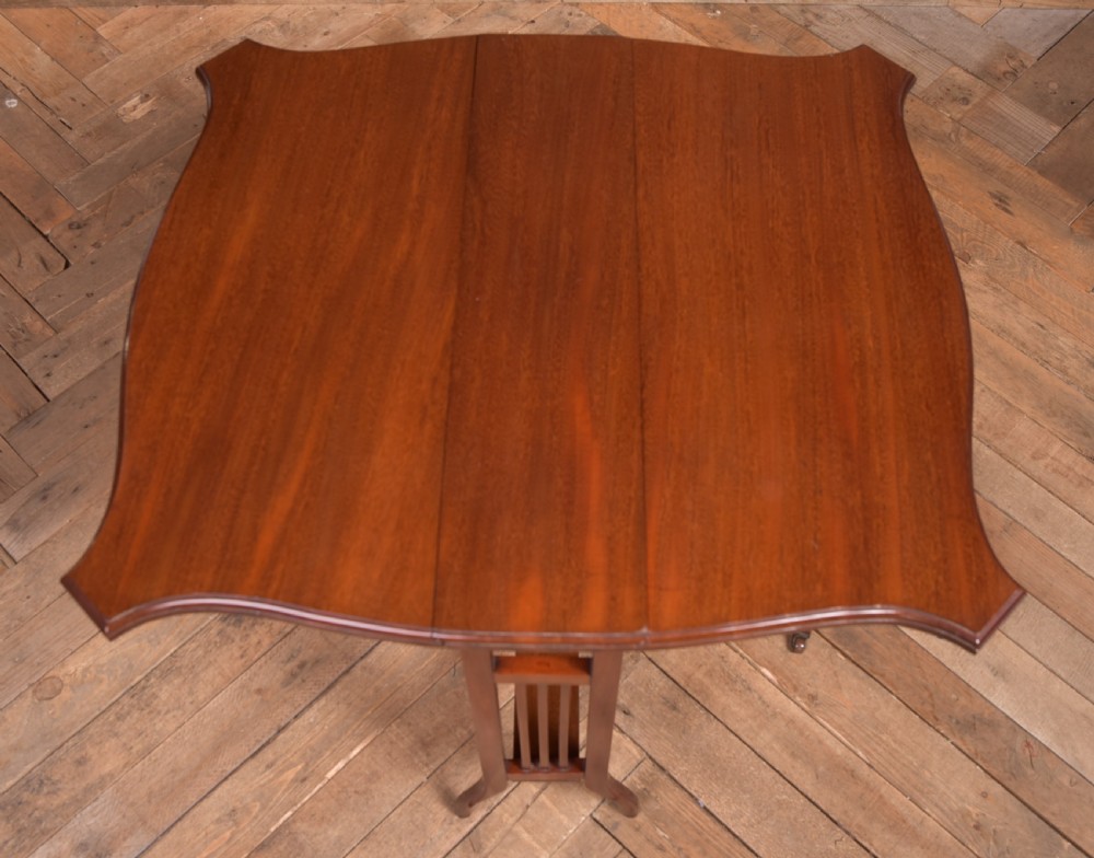 An Edwardian mahogany Sutherland side table shown in a folded state with deep drop leaves, slatted end supports, and curved legs with brass castors. View X