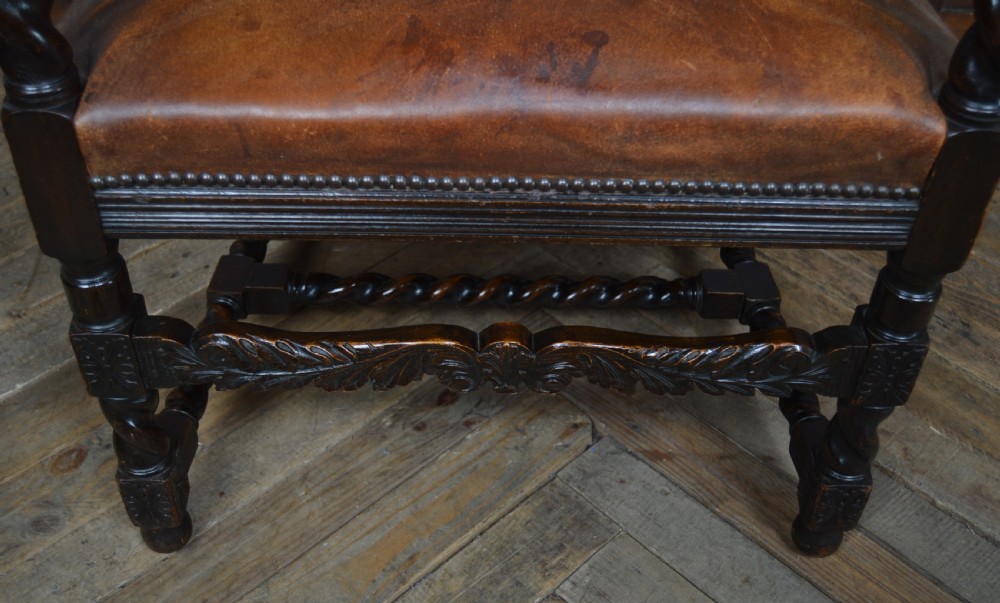 A Victorian Jacobean Revival carved oak armchair featuring barley twist uprights, aged brown leather upholstery with stud detail, and elaborate foliate cresting. View IX