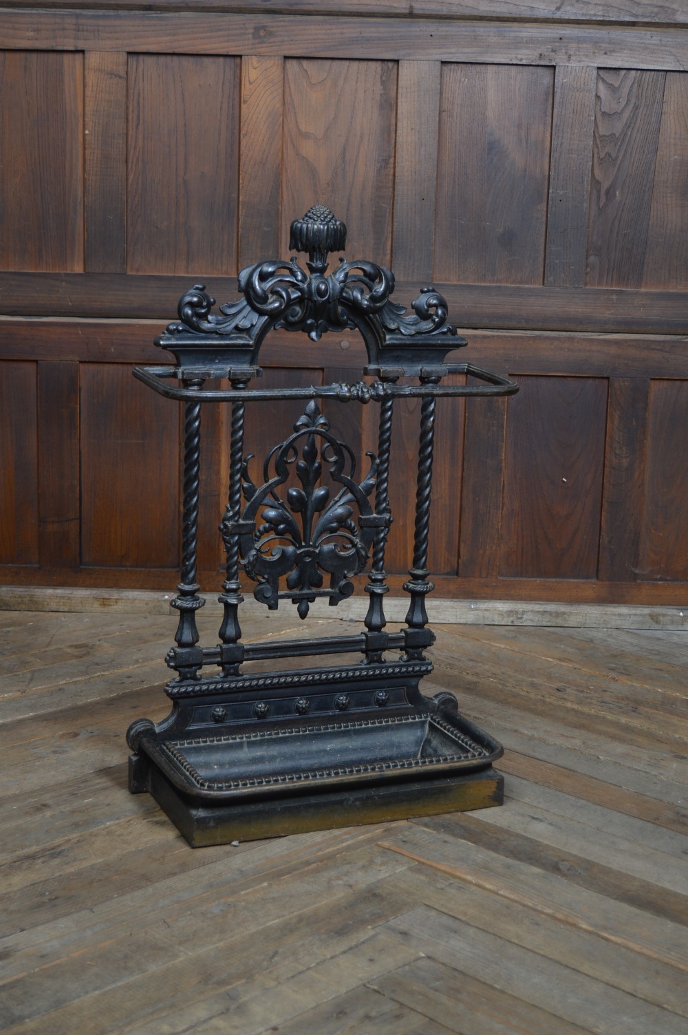 An ornate black Victorian cast iron stick stand featuring rope twist supports, central foliate scrollwork, and a drip tray at the base. View II