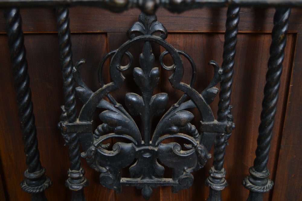 An ornate black Victorian cast iron stick stand featuring rope twist supports, central foliate scrollwork, and a drip tray at the base. View VI