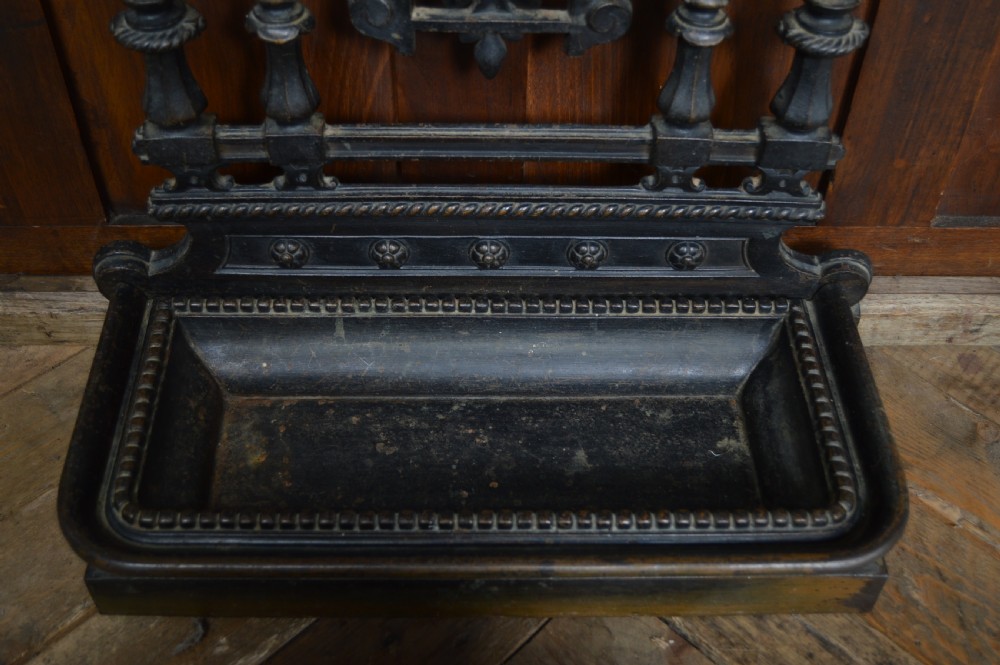 An ornate black Victorian cast iron stick stand featuring rope twist supports, central foliate scrollwork, and a drip tray at the base. View VII