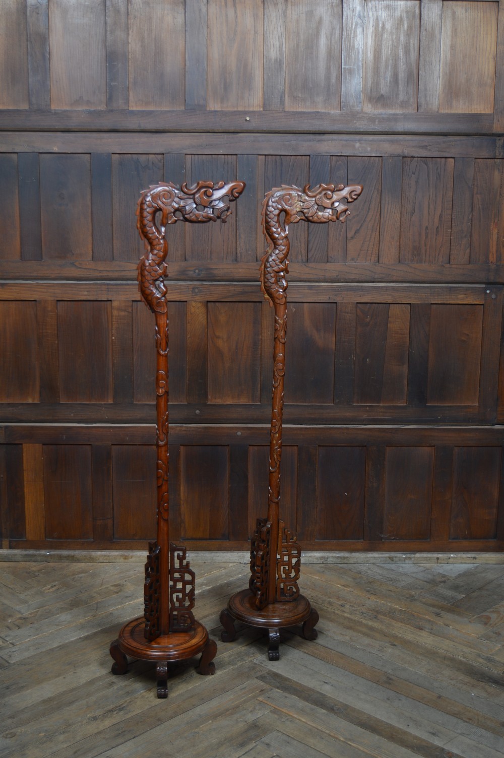 A pair of tall carved hardwood Chinese lantern stands featuring carved dragon head finials, open fretwork, and circular bases.