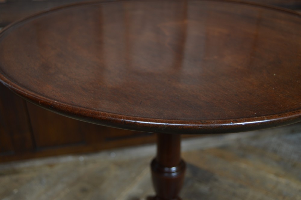 An antique mahogany wine table featuring a circular top with a raised dished edge on a turned pedestal stem with three splayed tripod legs. View VI
