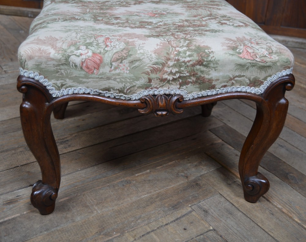 A low Victorian rosewood footstool featuring carved cabriole legs with scroll feet and a rectangular upholstered seat covered in a pastoral pattern textile. View II