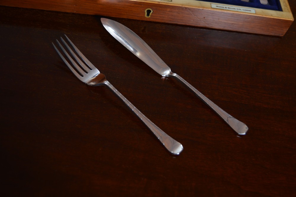 An open wooden canteen displaying a 12-person silver-plated fish cutlery set fitted against a deep blue velvet lining. View XII