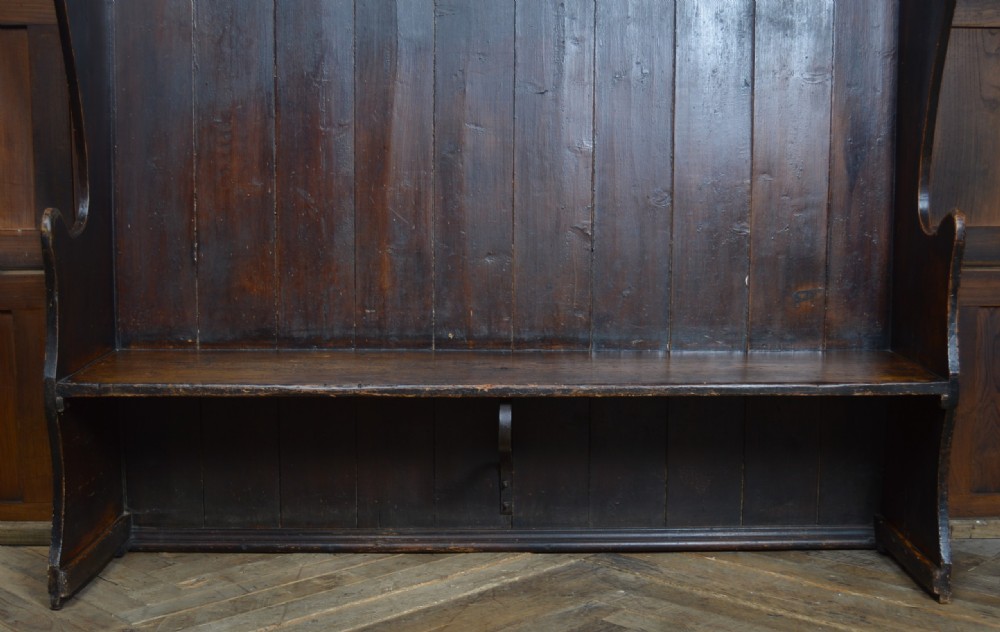 An early nineteenth-century dark-stained pine settle featuring a tall vertical-plank high back, winged sides, and a simple wooden bench seat. View III