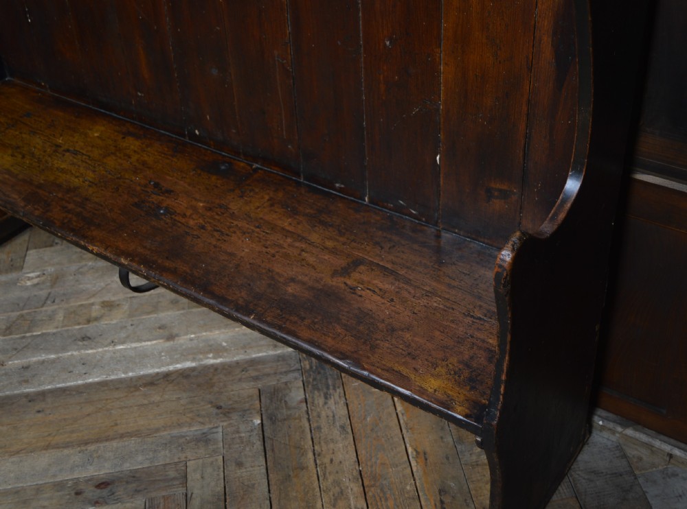 An early nineteenth-century dark-stained pine settle featuring a tall vertical-plank high back, winged sides, and a simple wooden bench seat. View VI