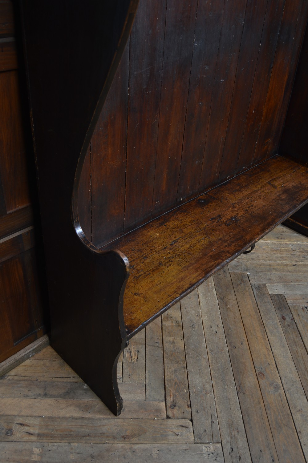 An early nineteenth-century dark-stained pine settle featuring a tall vertical-plank high back, winged sides, and a simple wooden bench seat. View VIII