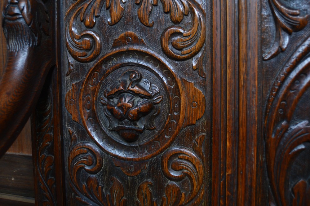 A heavily carved dark oak monks bench featuring Green Man foliate face motifs, ornate scrollwork, a raised back panel, and a hinged lid seat. View XIII