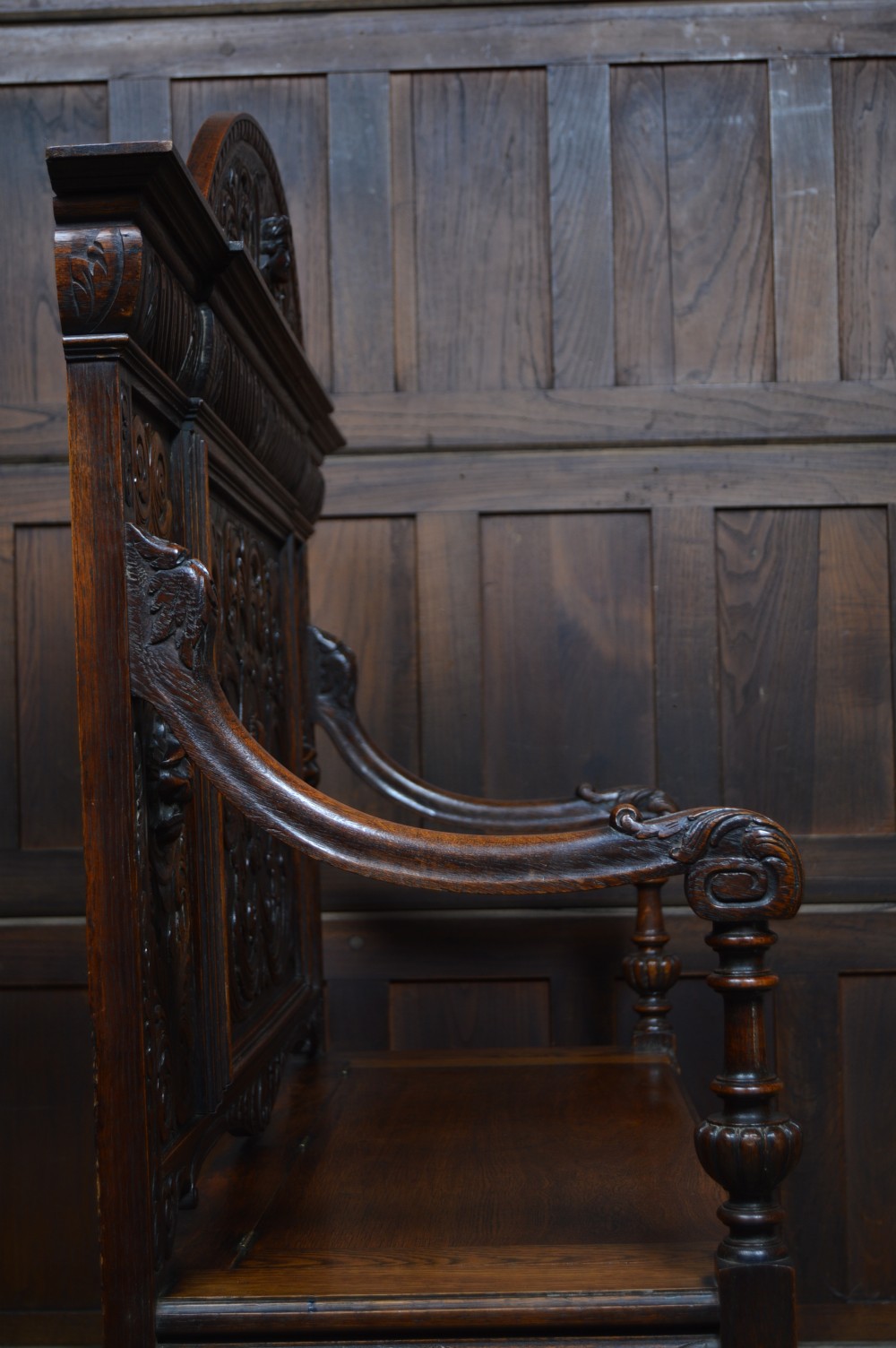 A heavily carved dark oak monks bench featuring Green Man foliate face motifs, ornate scrollwork, a raised back panel, and a hinged lid seat. View XIX