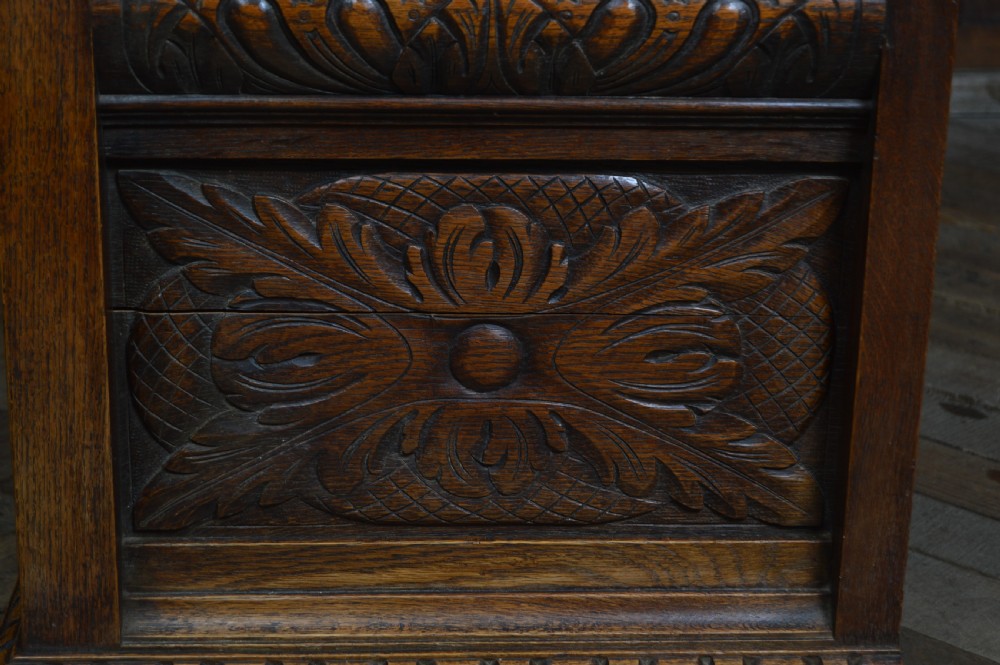A heavily carved dark oak monks bench featuring Green Man foliate face motifs, ornate scrollwork, a raised back panel, and a hinged lid seat. View XXIII