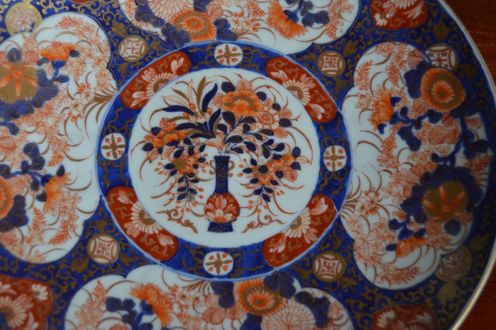A circular Japanese Imari porcelain plate decorated with hand-painted cobalt blue, rust red, and gold floral patterns surrounding a central floral vase motif. View II