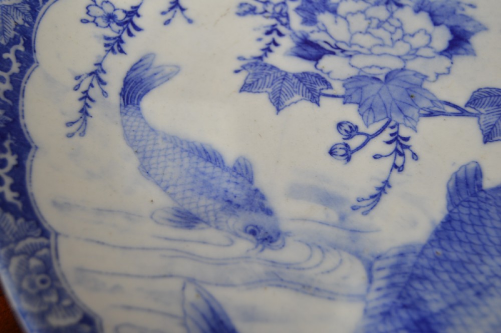 A circular blue and white porcelain charger decorated with hand-painted carp fish, birds, and floral foliage inside a geometric patterned border. View III