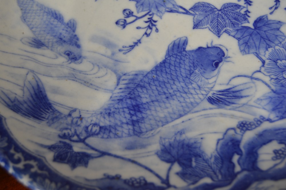 A circular blue and white porcelain charger decorated with hand-painted carp fish, birds, and floral foliage inside a geometric patterned border. View V